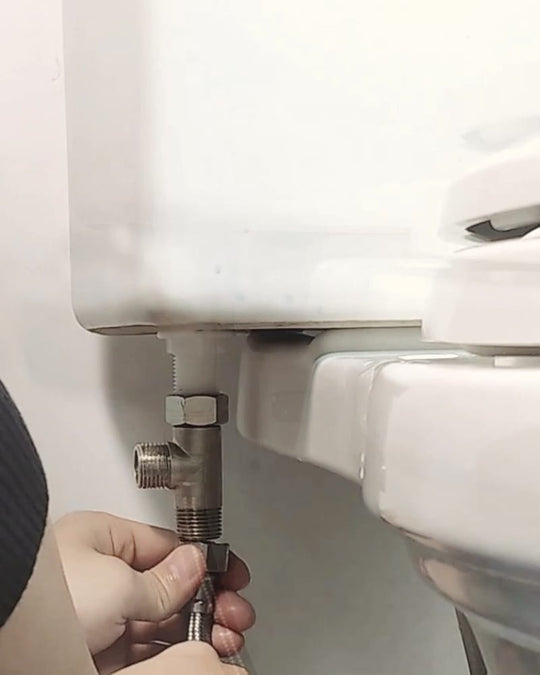 Deux mains vissent le flexible sur le raccord en T posé sous le réservoir des WC.